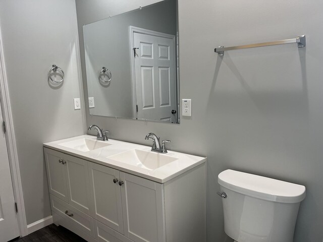 full bathroom featuring toilet, double vanity, a sink, and wood finished floors