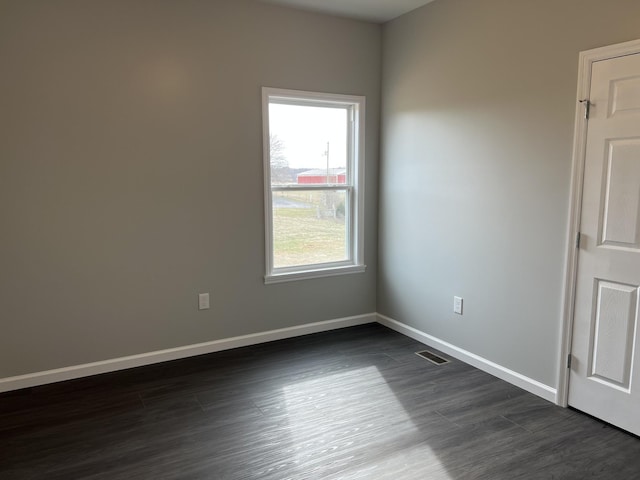 empty room with dark wood-type flooring, visible vents, and baseboards