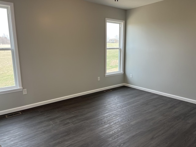 unfurnished room with baseboards, visible vents, and dark wood finished floors