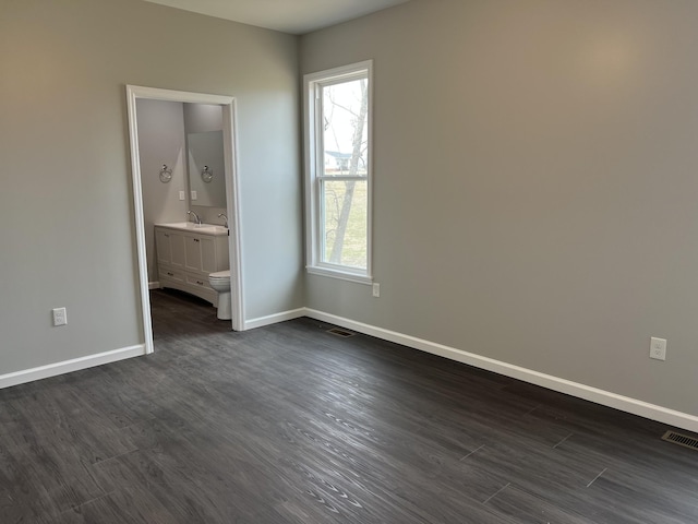 unfurnished bedroom featuring dark wood-style floors, multiple windows, a sink, and baseboards