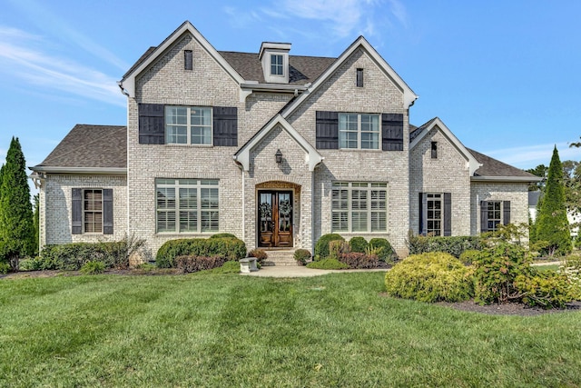 view of front facade featuring french doors, roof with shingles, a front yard, and brick siding