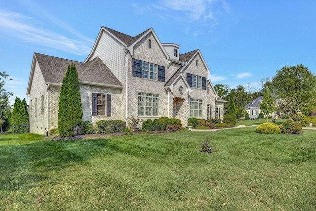 view of front of house featuring brick siding, roof with shingles, and a front yard