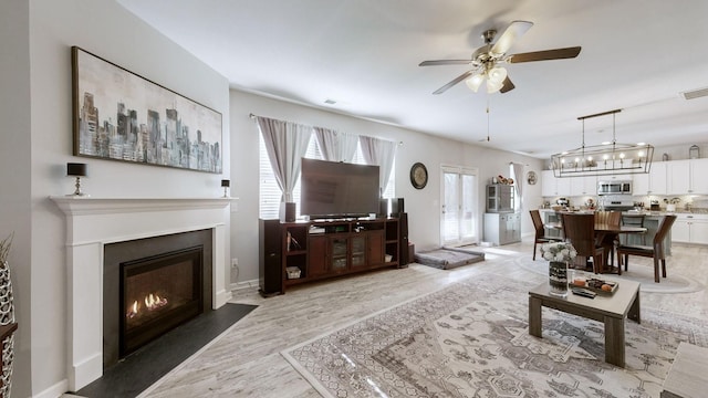 living room featuring baseboards, visible vents, a ceiling fan, a fireplace with flush hearth, and wood finished floors