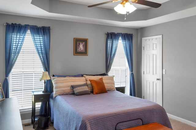 carpeted bedroom with a ceiling fan, a raised ceiling, visible vents, and baseboards