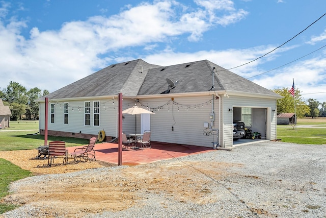 back of house with a garage, a shingled roof, a yard, driveway, and a patio area