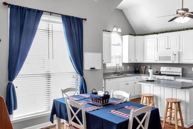 kitchen with white appliances, dark countertops, a center island, white cabinetry, and a sink