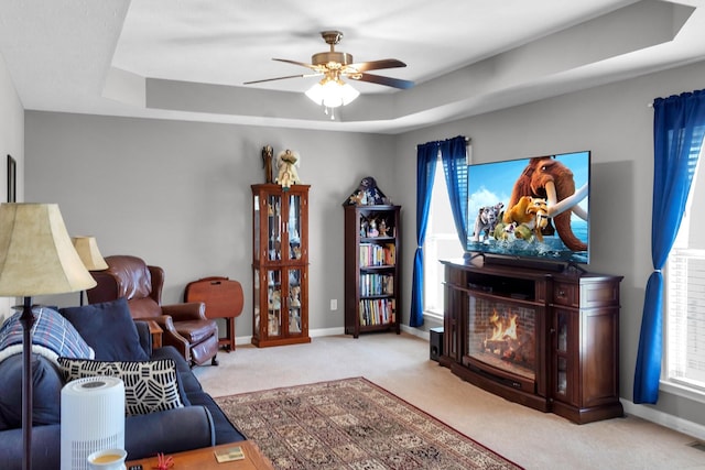 living area featuring a tray ceiling, light colored carpet, a lit fireplace, and baseboards