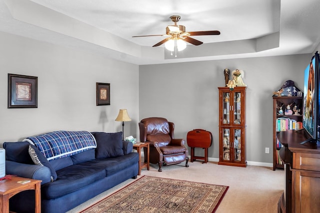 living area with ceiling fan, baseboards, a raised ceiling, and light colored carpet