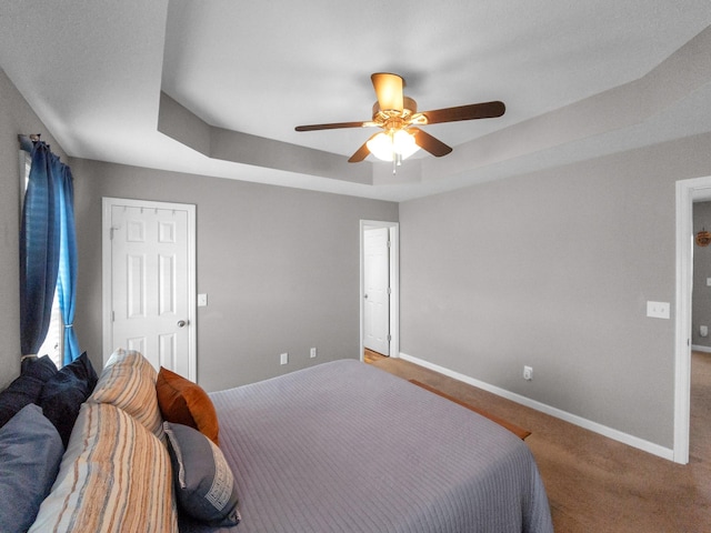 carpeted bedroom with ceiling fan, a tray ceiling, and baseboards