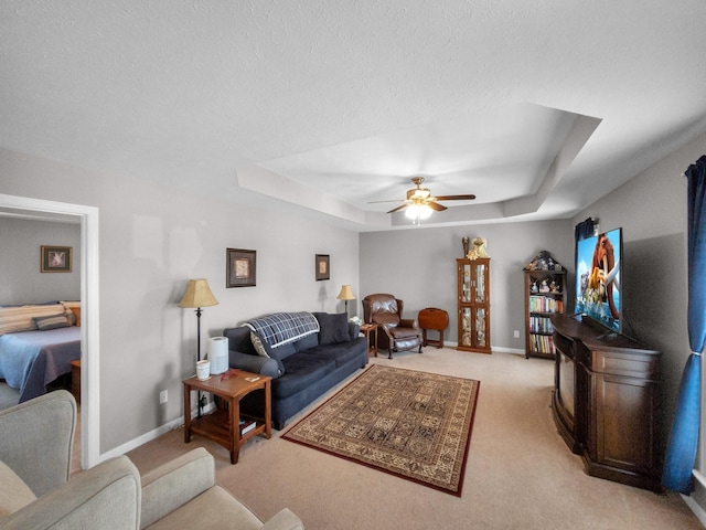 living area with ceiling fan, a textured ceiling, light carpet, baseboards, and a tray ceiling