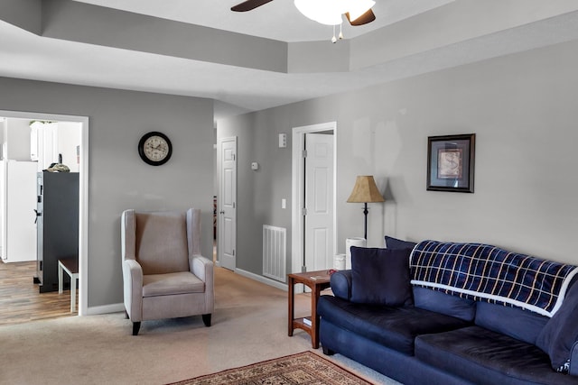 living room featuring carpet floors, a tray ceiling, visible vents, ceiling fan, and baseboards