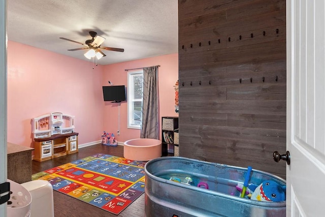 playroom featuring ceiling fan, baseboards, and dark wood finished floors