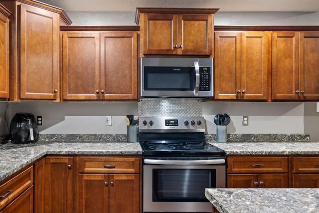 kitchen featuring appliances with stainless steel finishes, tasteful backsplash, brown cabinetry, and light stone countertops