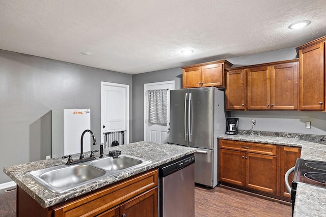 kitchen featuring a center island with sink, dark wood finished floors, brown cabinetry, stainless steel appliances, and a sink