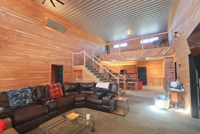 carpeted living area featuring wooden walls, a towering ceiling, and stairs