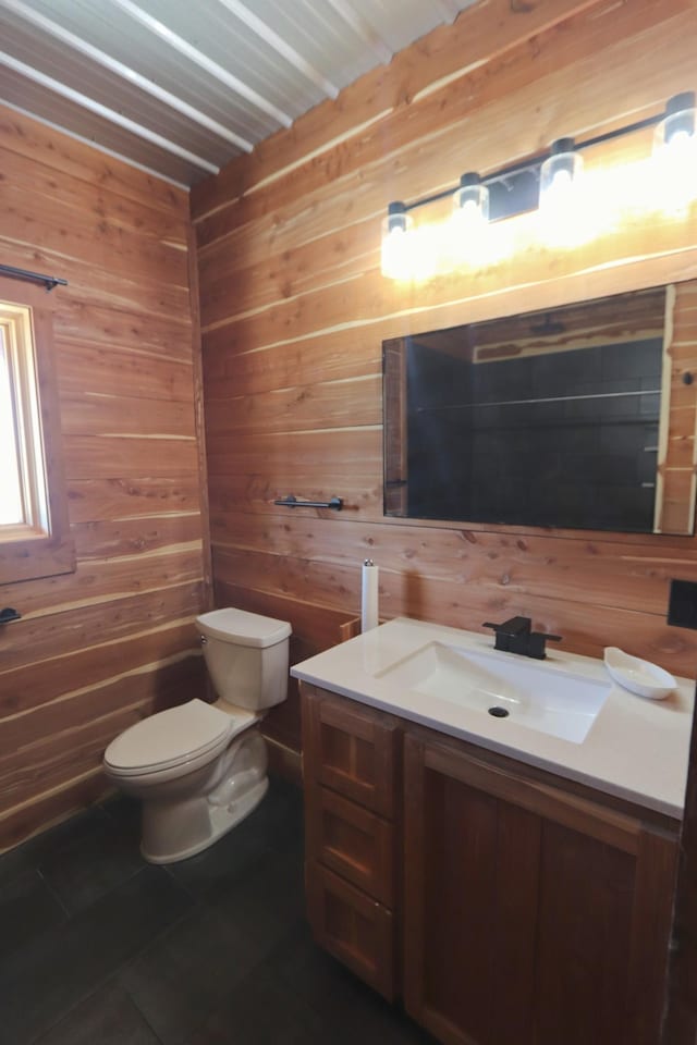 half bath featuring wooden walls, tile patterned flooring, vanity, and toilet