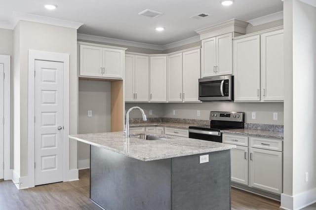 kitchen with a sink, white cabinetry, appliances with stainless steel finishes, light wood-type flooring, and an island with sink