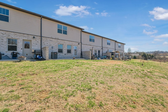 back of house with brick siding, a yard, and central AC unit