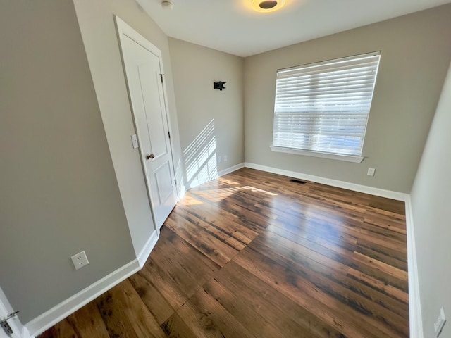 empty room featuring dark wood-type flooring, visible vents, and baseboards