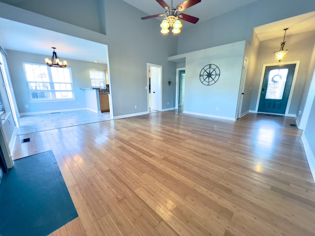 unfurnished living room featuring ceiling fan with notable chandelier, a high ceiling, wood finished floors, visible vents, and baseboards