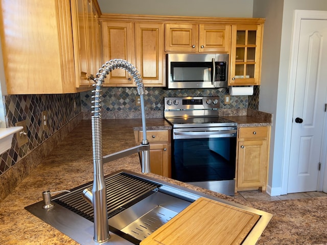 kitchen featuring appliances with stainless steel finishes, glass insert cabinets, backsplash, and a sink