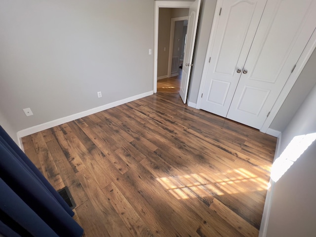 unfurnished bedroom featuring a closet, dark wood-style flooring, visible vents, and baseboards