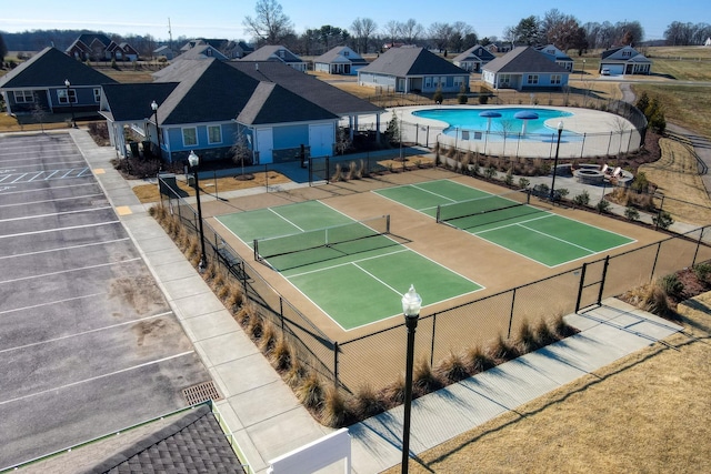 view of tennis court with a community pool, fence, and a residential view