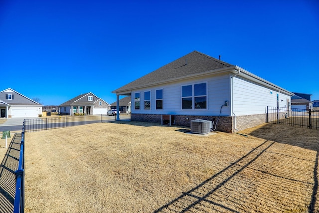 rear view of property featuring a residential view, central AC, fence, and roof with shingles