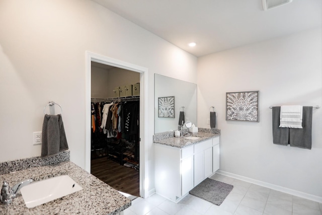 bathroom with two vanities, visible vents, a walk in closet, and a sink