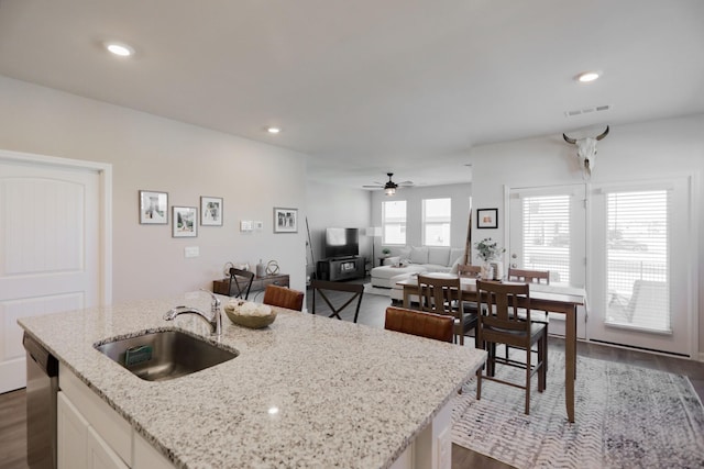 kitchen with a center island with sink, stainless steel dishwasher, white cabinets, a sink, and light stone countertops