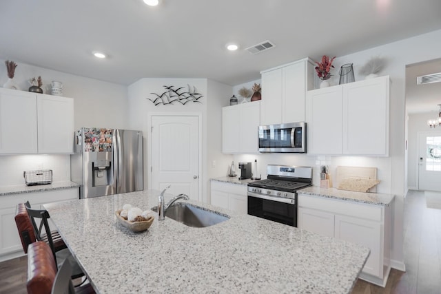 kitchen featuring visible vents, white cabinets, an island with sink, stainless steel appliances, and a sink