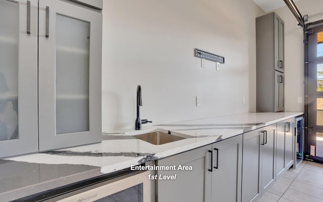 kitchen with light stone counters, wine cooler, light tile patterned floors, gray cabinetry, and a sink