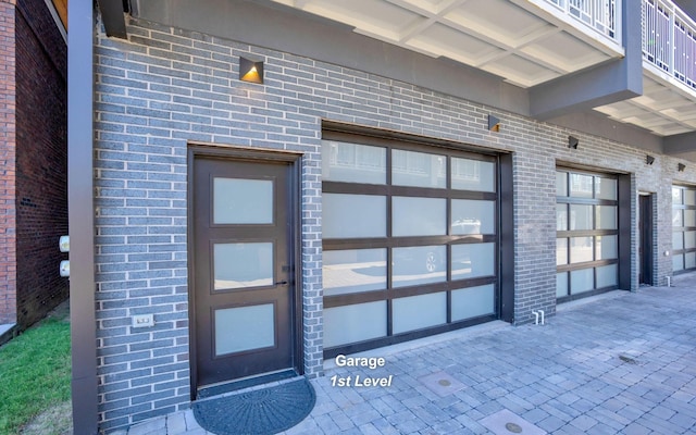 entrance to property featuring a garage and brick siding