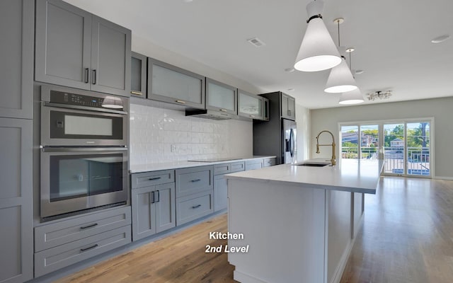 kitchen with decorative light fixtures, stainless steel appliances, a sink, light countertops, and a center island with sink