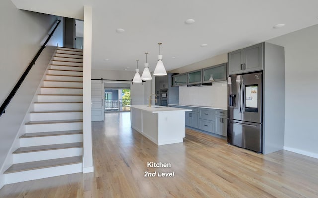 kitchen featuring a barn door, decorative light fixtures, light countertops, black appliances, and a center island with sink