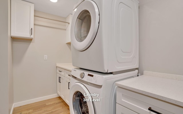 washroom featuring light wood-type flooring, stacked washer and dryer, baseboards, and cabinet space