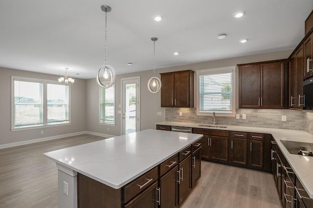 kitchen with light wood-style flooring, decorative light fixtures, a center island, black electric stovetop, and a sink