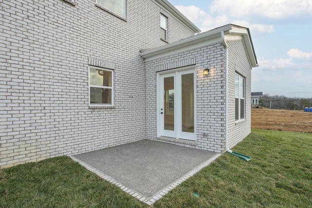 view of exterior entry with brick siding, a lawn, and a patio area