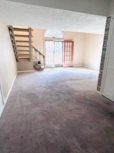 unfurnished living room with carpet flooring, a textured ceiling, baseboards, and stairs