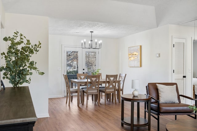 dining space featuring french doors, a notable chandelier, a textured ceiling, wood finished floors, and baseboards