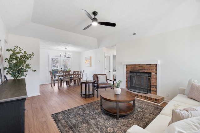 living area with a textured ceiling, wood finished floors, visible vents, baseboards, and a brick fireplace