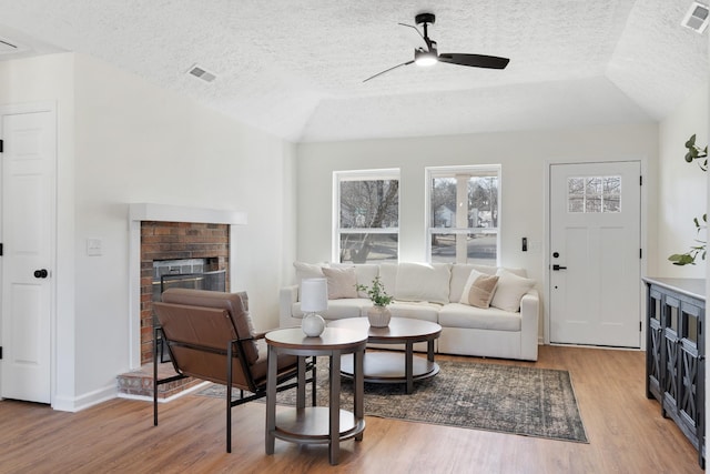 living area with lofted ceiling, a fireplace, visible vents, a ceiling fan, and light wood finished floors