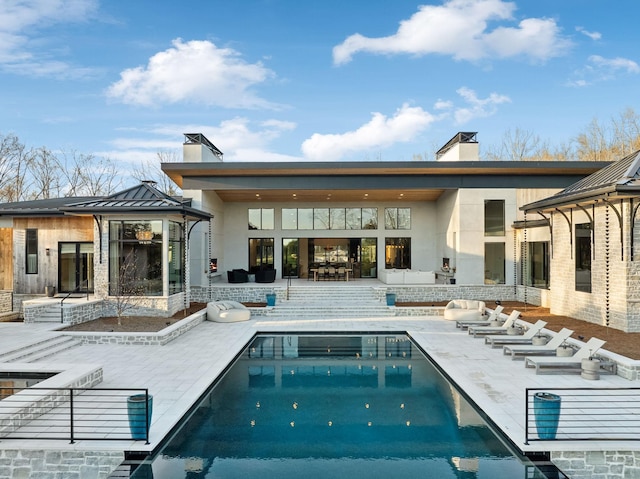 rear view of house featuring a standing seam roof, a patio area, an outdoor pool, and a chimney