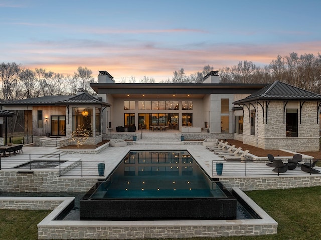 back of house with a patio area, metal roof, a standing seam roof, and a chimney