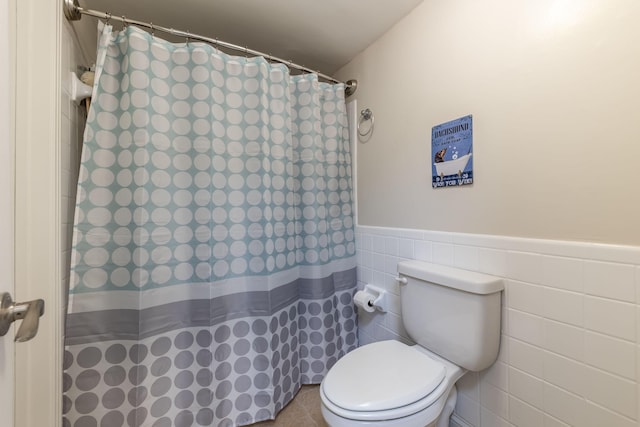 full bath with a wainscoted wall, a shower with shower curtain, toilet, and tile walls