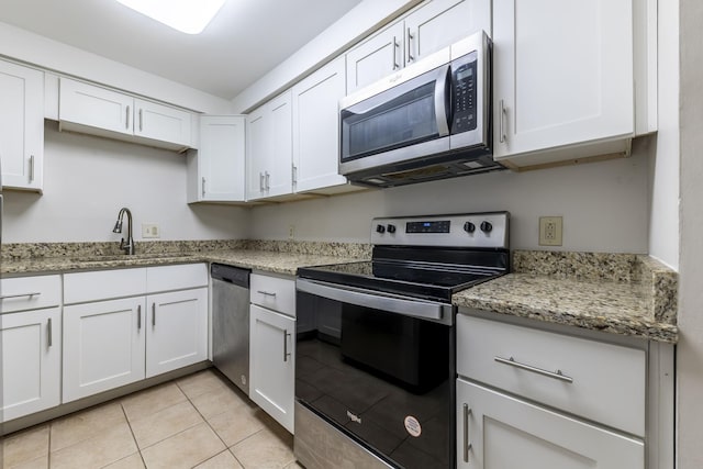 kitchen with light stone counters, appliances with stainless steel finishes, a sink, and white cabinetry