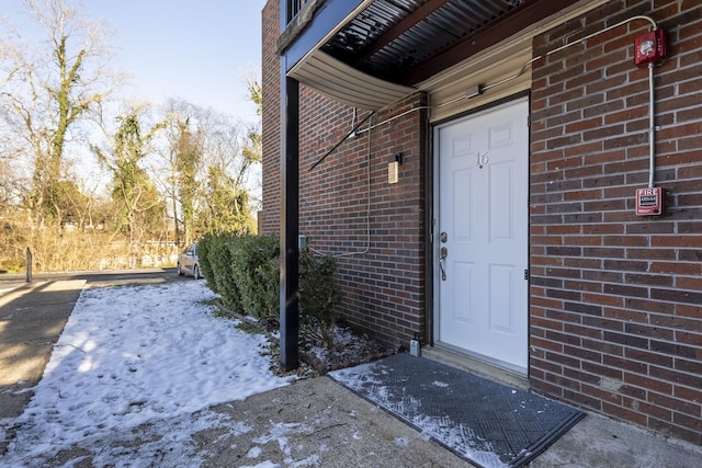 snow covered property entrance featuring brick siding