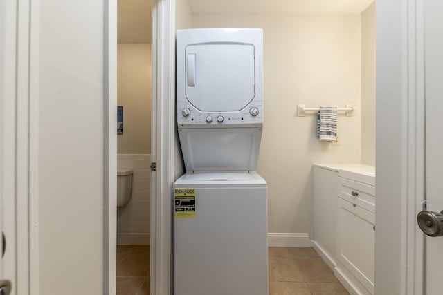 laundry area with stacked washing maching and dryer and light tile patterned floors