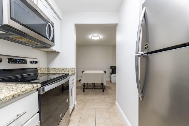 kitchen with light stone counters, light tile patterned floors, stainless steel appliances, white cabinetry, and baseboards