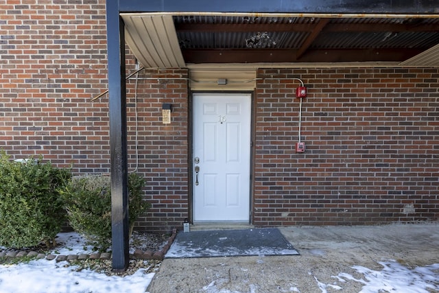 snow covered property entrance featuring brick siding